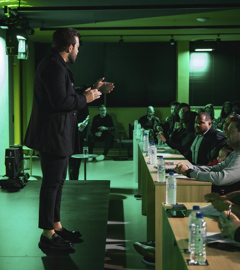 Renan Nicolini sobre o palco conversando com empresários sentados à mesa, durante uma mentoria