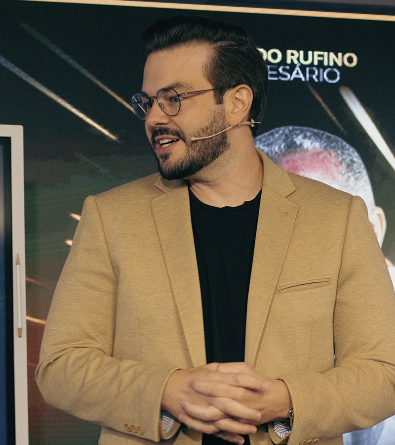 Renan Nicolini de blazer claro, falando de perfil durante uma palestra