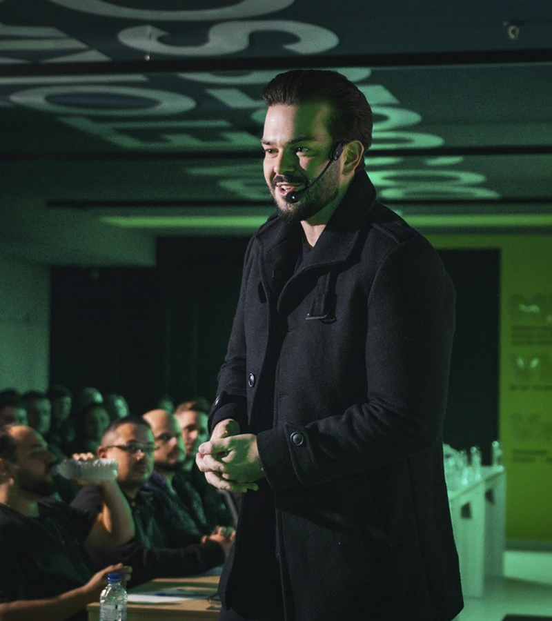Renan Nicolini falando em pé para uma plateia de empresários, em sala com iluminação verde